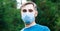 Caucasian man in medical face mask outside. Guy portrait in protective blue mask in park alone. Protection against coronavirus,