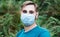 Caucasian man in medical face mask outside. Guy portrait in protective blue mask in park alone. Protection against coronavirus,