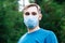 Caucasian man in medical face mask outside. Guy portrait in protective mask in park alone. Protection against coronavirus,