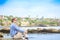 Caucasian man, mid forties sitting by rocky cliff near water