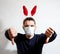 Caucasian man with red hare ears wears medical protective mask and puts dislike with both hands. Celebrate Easter in self