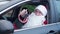 Caucasian man in red Santa costume boasting car keys sitting on driver's seat in vehicle outdoors. Portrait of Father