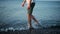 Caucasian man in shorts walks slowly in shallow water of pebble beach.