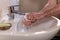 Caucasian man thoroughly cleaning hands and fingernails with a brush in wash basin under running water tap. Personal hygiene