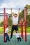 Caucasian man and two boys doing exercises outdoors. The father pulls himself up on the horizontal bar with his sons on