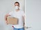 Caucasian man wearing respirator with cardboard box opens the door and enters the room