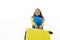 Caucasian mischievous child girl in blue jacket, going for vacations, carrying heavy yellow valise, on white background