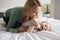 Caucasian mother kneeling on bed, tickling her baby daughter