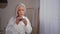 Caucasian old senior mature woman lady 60s grandmother model in bathrobe in bath touching gray long smooth thin hair