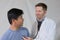 Caucasian physician listening to Asian patient\'s heart