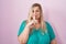 Caucasian plus size woman standing over pink background asking to be quiet with finger on lips