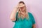 Caucasian plus size woman standing over pink background covering eyes with hand, looking serious and sad