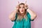 Caucasian plus size woman standing over pink background doing funny gesture with finger over head as bull horns