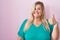 Caucasian plus size woman standing over pink background doing happy thumbs up gesture with hand