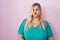 Caucasian plus size woman standing over pink background puffing cheeks with funny face