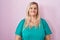 Caucasian plus size woman standing over pink background relaxed with serious expression on face