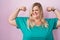 Caucasian plus size woman standing over pink background showing arms muscles smiling proud