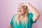 Caucasian plus size woman standing over pink background very happy and smiling looking far away with hand over head
