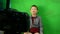 Caucasian preschooler boy sitting against a green background writes a blog in front of a video camera. Online course recording. Ch