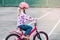 Caucasian preschooler girl riding pink bike bicycle in helmet on backyard road outside on spring summer day.