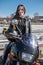 Caucasian pretty girl motorcyclist looking at camera, sits on motorbike, holding hands black helmet with yellow funny ears
