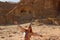 Caucasian red-haired hippie woman traveler in glasses joyfully spread her hand against a sandy rock in Timna National Park, Israel