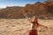 Caucasian red-haired hippie woman traveler in glasses joyfully spread her hand against a sandy rock in Timna National Park, Israel