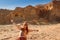 Caucasian red-haired hippie woman traveler in glasses joyfully spread her hand against a sandy rock in Timna National Park, Israel