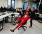 Caucasian red-haired woman, bearded caucasian man rolled African American young woman on office chair. Colleagues have