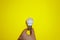 Caucasian\\\'s hand hold white eco lamp bulb isolated on yellow background. Business concept. Copy space place