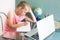 Caucasian school girl is doing homework at home in front of a laptop.