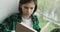 Caucasian Schoolboy Immersed in a Book on the Windowsill