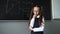 Caucasian schoolgirl in glasses stands thinking at the blackboard and remembers the answer.