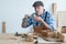 Caucasian senior old white bearded man carpenter in apron and hat working in workshop, use sandpaper polishing and blowing dust