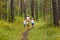 A Caucasian slender smiling woman and two pre-school children in white t-shirts run along the path, holding hands in the summer