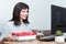 Caucasian smiling woman sitting in front of a monitor holding cash and a red gift box. Online shopping at home