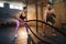 Caucasian sport woman doing battle rope exercise under control of trainer in gym.