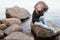 Caucasian teenage girl sitting on coastal stones