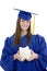 Caucasian teenager wearing blue graduation gown and holding piggy bank