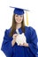 Caucasian teenager wearing blue graduation gown and holding piggy bank