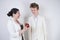 Caucasian teenager in a white business suit stands next to friendly adult asian woman and holds a phone on a white background