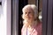 Caucasian thoughtful senior woman with wavy hair looking away by window at nursing home