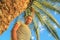 Caucasian white male traveler with long hair and beard stands next to palm tree