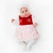 Caucasian White newborn baby girl in a dress with ruffles on a pink background with a flowers bandage on her head.