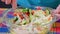 caucasian woman adding white sauce in glass bowl with vegetable salad and mixing it with steel spoon