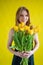 Caucasian woman with an armful of yellow tulips on a yellow background. International Women`s Day. Bouquet of spring