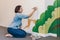 Caucasian woman artist hand painting murals on walls indoor at apartment or studio school with acrylic paints. Lifestyle creative