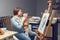 Caucasian woman artist holding stroking cat pet while sitting at home art studio by drawing easel. Lifestyle activity hobby.