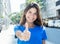 Caucasian woman in a blue shirt in the city showing thumb up