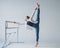 Caucasian woman in casual clothes pulls the split at the ballet barre.